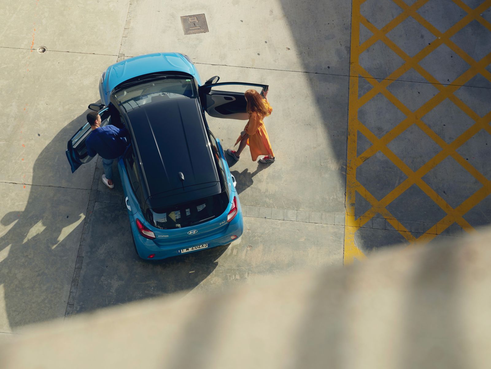 Pohled shora - dvojice nasedá do svého modrého Hyundai i10.